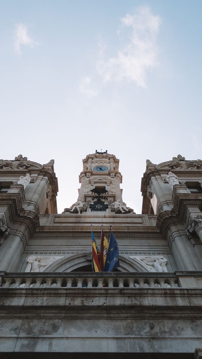 Services Low-angle view of Valencia City Hall facade featuring European Union and Valencian flags.
