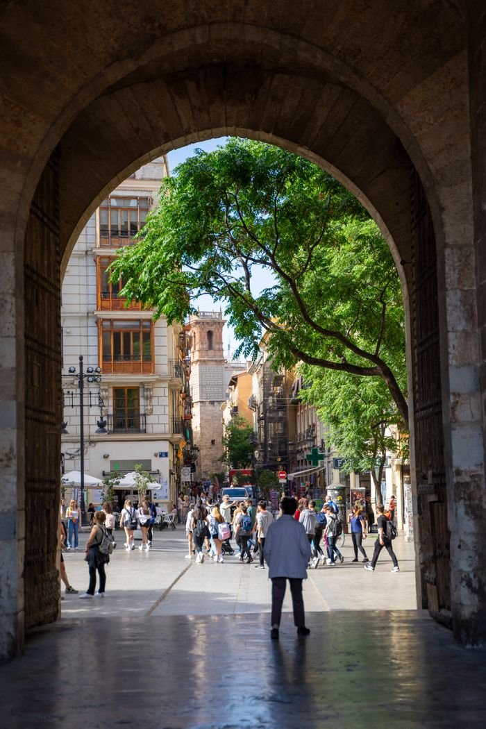 Services Charming street scene in Valencia, Spain, viewed through a historic archway with bustling activity.