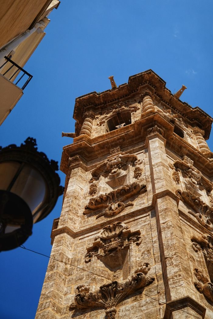 Services Ornate stone bell tower against a bright blue sky in Valencia, Spain.